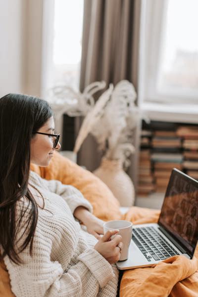 Woman wearing glasses sitting on a video call while holding a mug in her right hand.