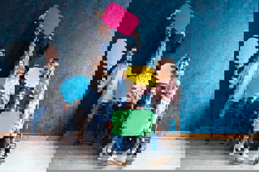 Five people sitting down smiling and holding cardboard cutouts of speech bubbles.