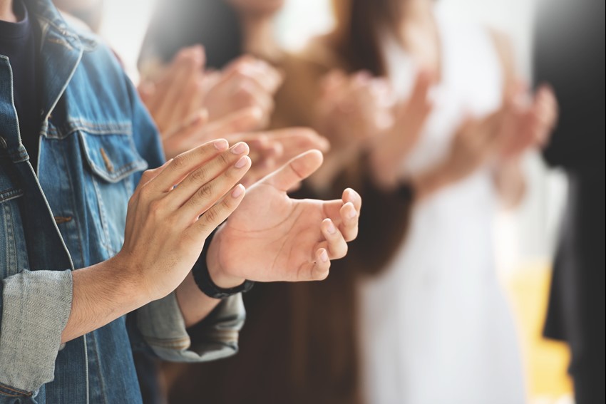 Close up picture of a group of people clapping.