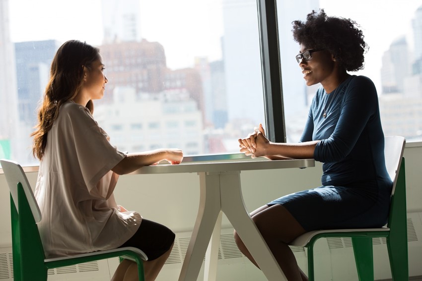 Two women sitting at a table having a one on one meeting.