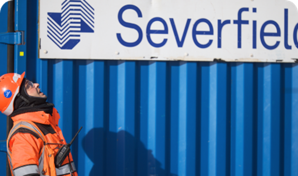 Employee in hardhat and work clothing looking up with blue Severfield branded crate in the background